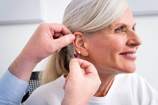 Ältere Frau bekommt modernes Hörgerät ins Ohr eingesetzt, Hörgeräte Beratung Seniorin.